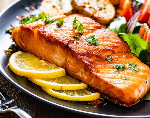 Fried salmon steak with lemon slices and salad on a plate for lunch.