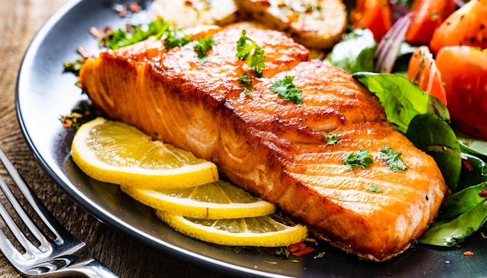 Fried salmon steak with lemon slices and salad on a plate for lunch.