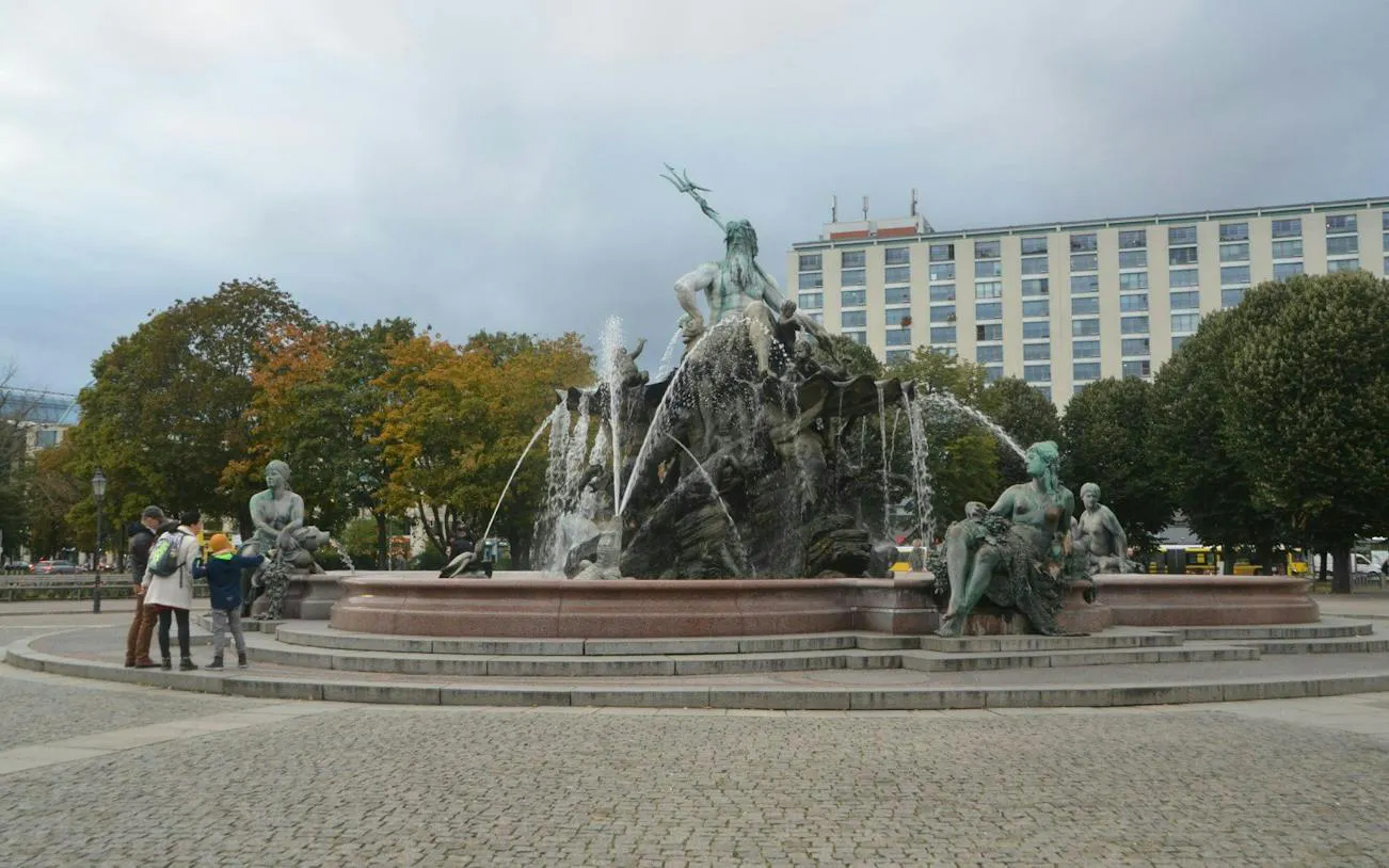 Neptune Fountain in Berlin with statues and tourists nearby.