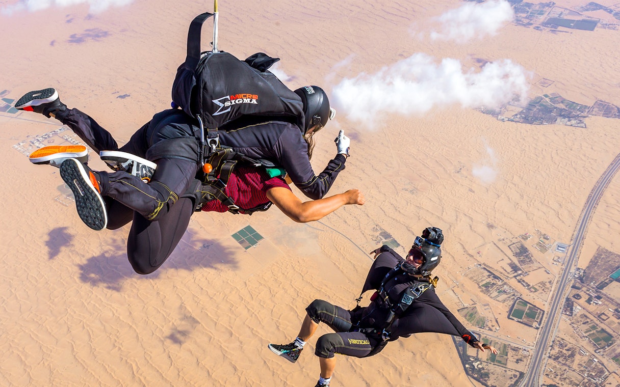 Skydivers over desert drop zone, one posing for a cameraman.