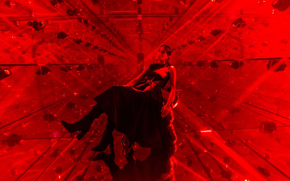 Person sitting in a red-lit mirrored room at AYA Universe.