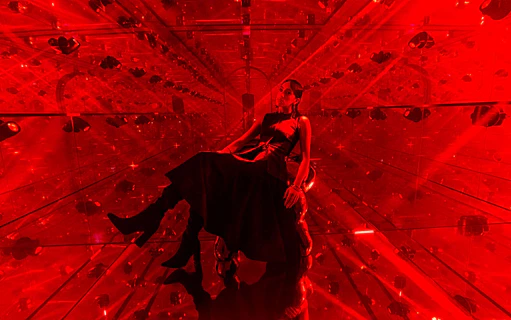Person sitting in a red-lit mirrored room at AYA Universe.
