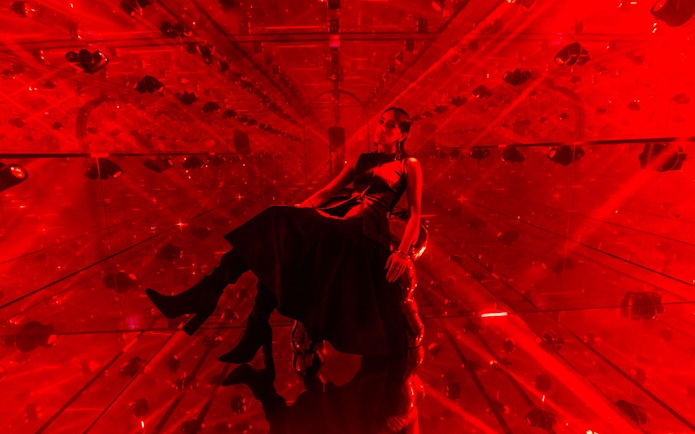 Person sitting in a red-lit mirrored room at AYA Universe.