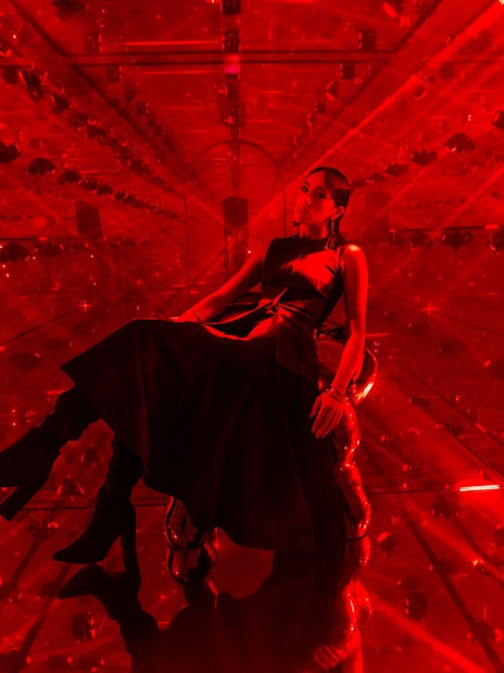 Person sitting in a red-lit mirrored room at AYA Universe.