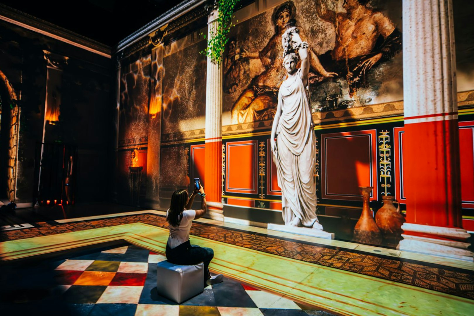 Interactive exhibit of ancient Pompeii with statue and fresco, visitor taking photo.
