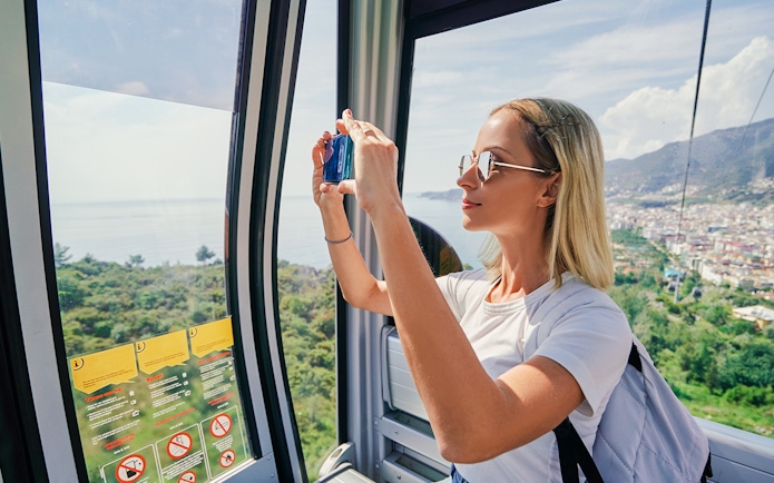 Woman taking photos inside a cable car overlooking Spanish landscape.
