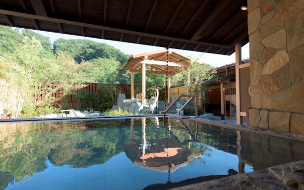 Keio Takaosan Onsen Gokurakuyu outdoor hot spring pool with wooden pavilion and lush greenery.