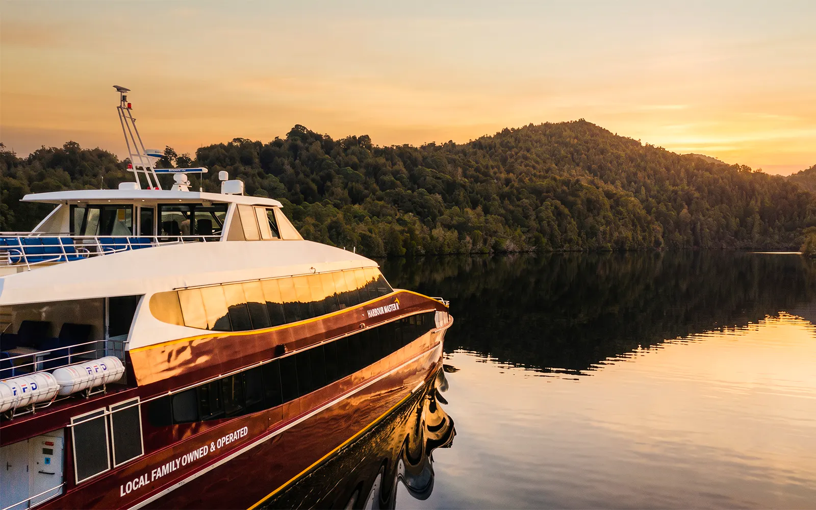Cruise boat on Gordon River at sunset, surrounded by lush forest near Strahan.