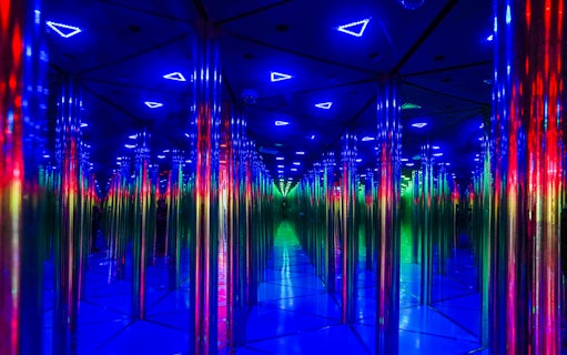 Tourists exploring colorful mirror maze with neon lights.
