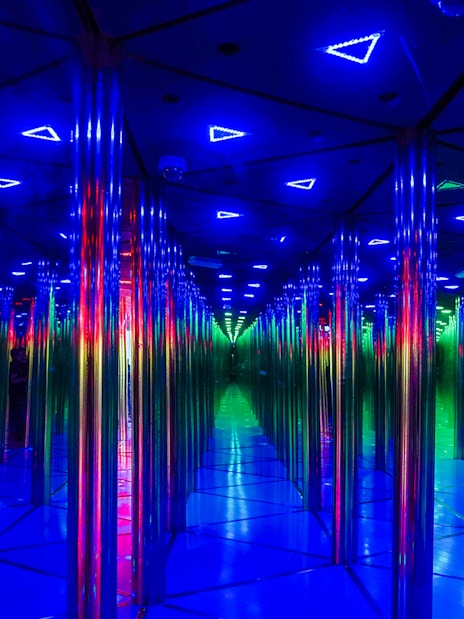 Tourists exploring colorful mirror maze with neon lights.