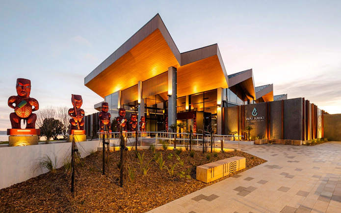 Wai Ariki Hot Springs & Spa entrance with Maori carvings at sunset.