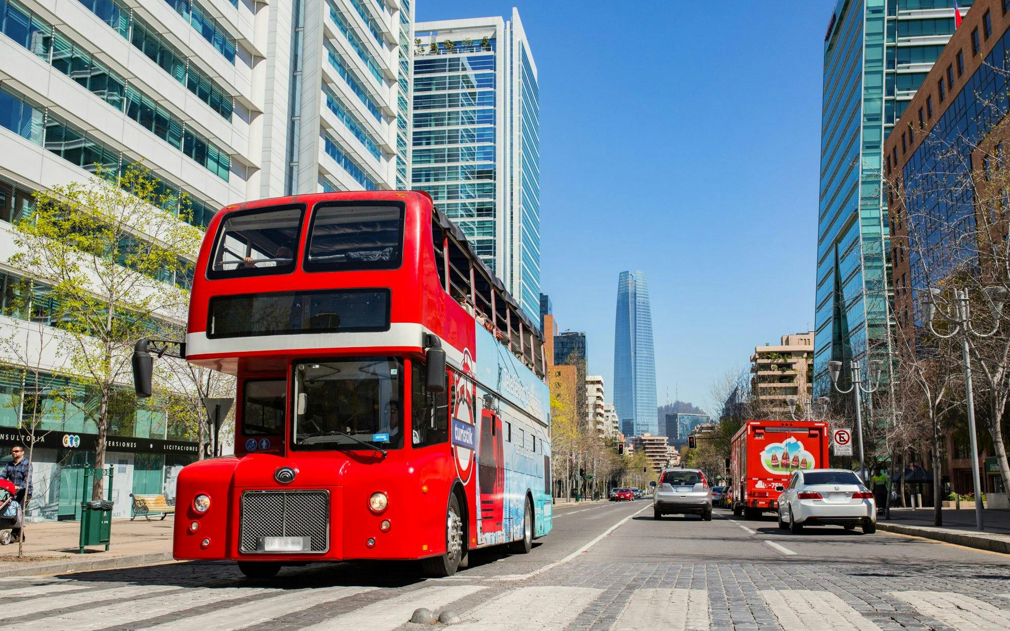 Turistik Hop-On Hop-Off bus on a street in Santiago, Chile with city skyline.