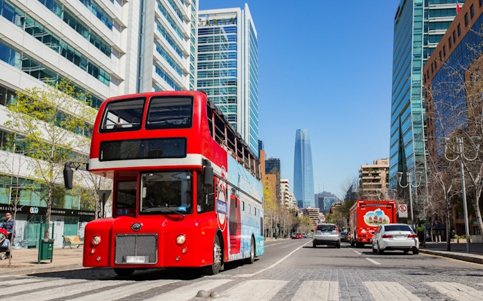 Turistik Hop-On Hop-Off bus on a street in Santiago, Chile with city skyline.