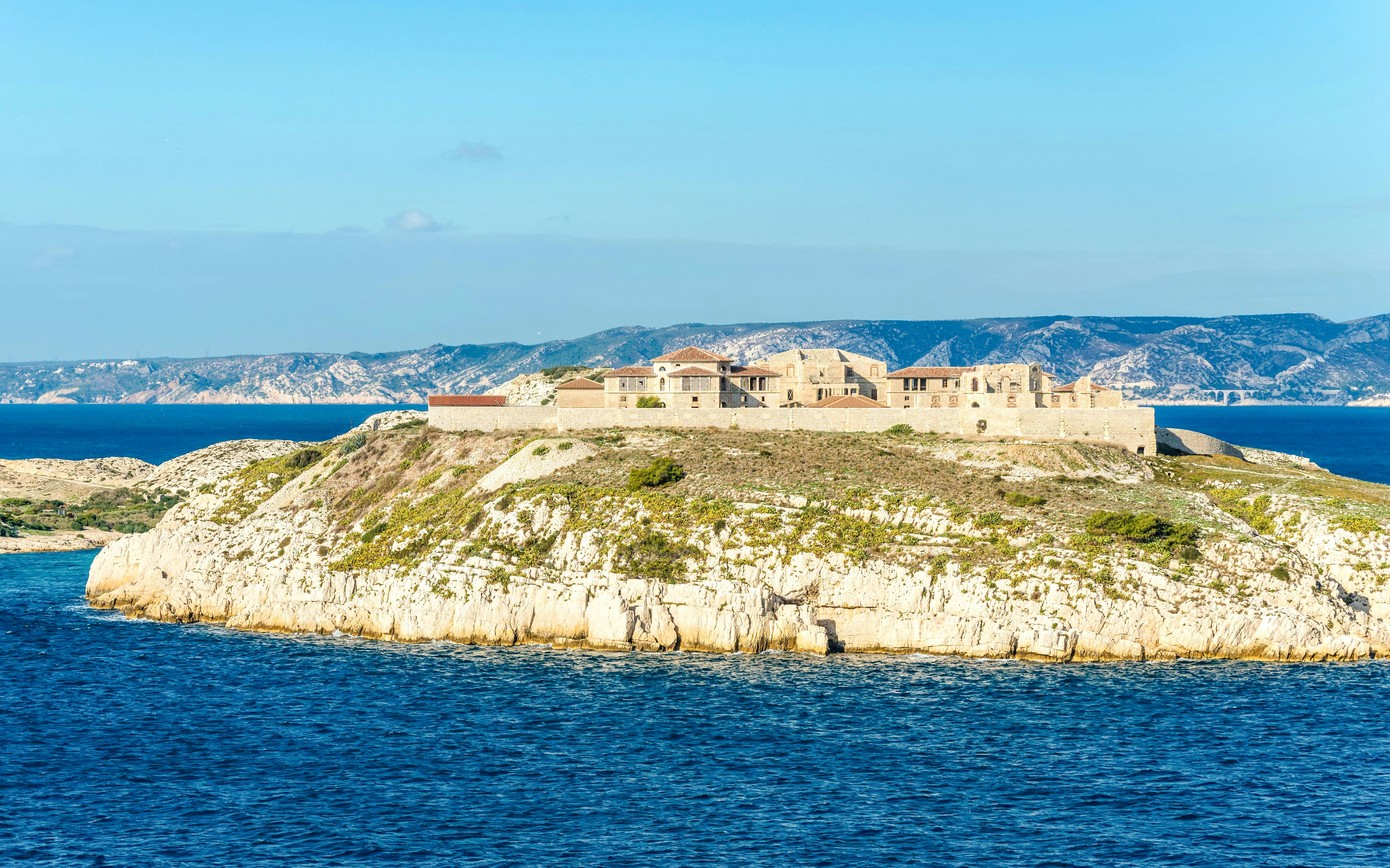 Historic fort on Ratonneau Island surrounded by blue sea and distant hills.