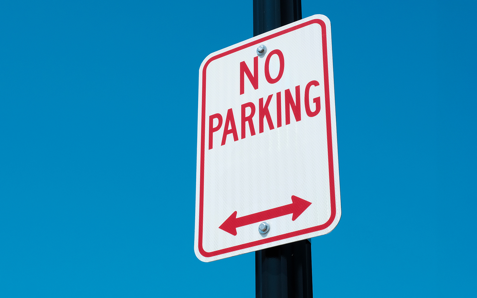 No parking sign with arrows on a road against a clear blue sky.