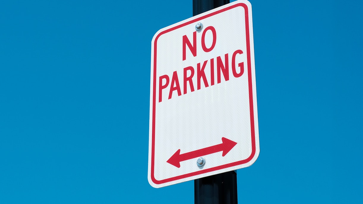 No parking sign with arrows on a road against a clear blue sky.