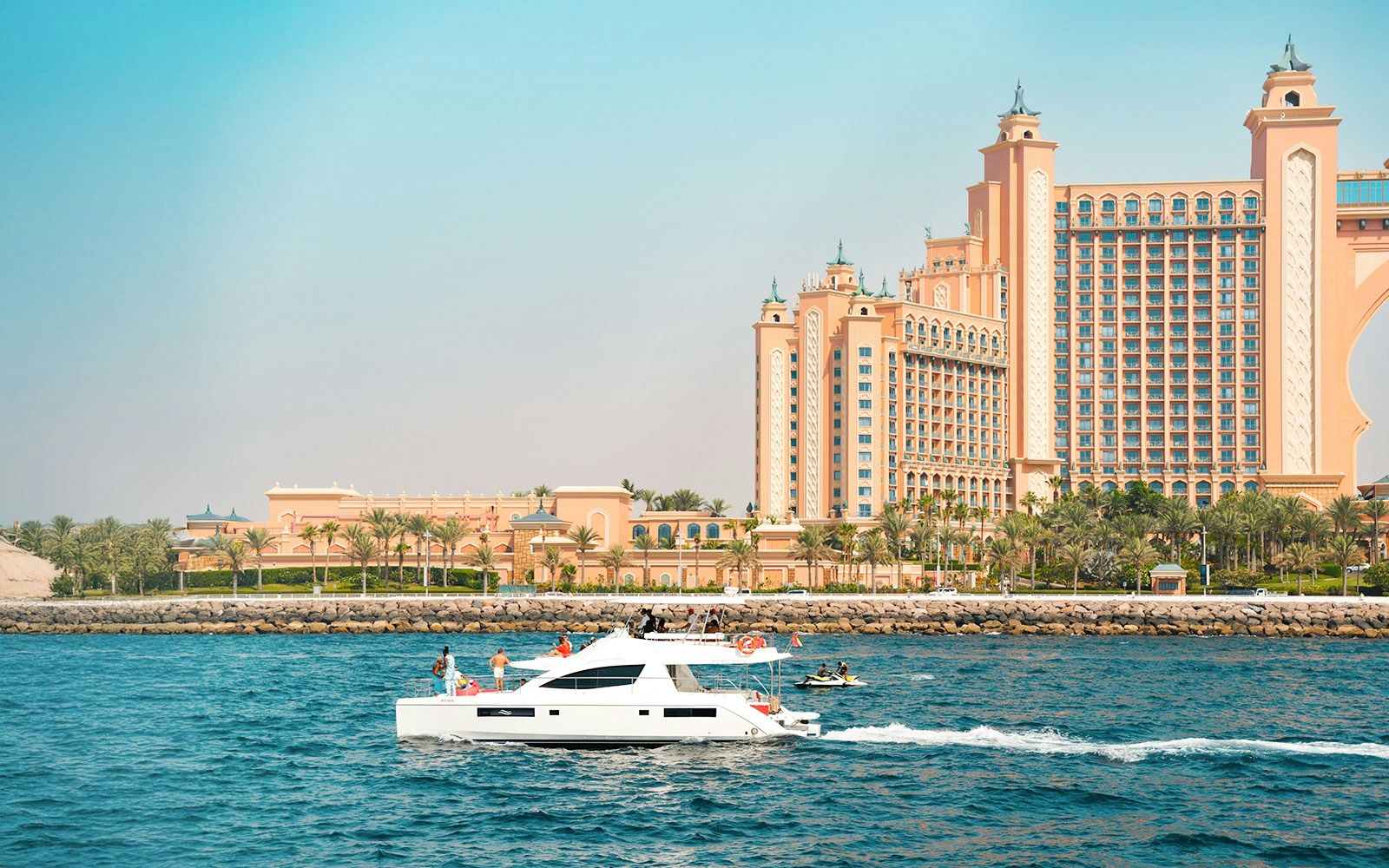 Luxury yacht cruising past Atlantis The Palm, Dubai, with guests enjoying the view.