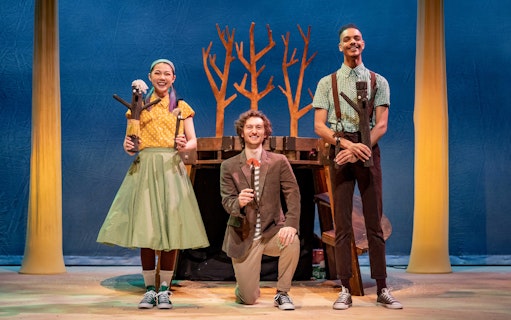 Performers on stage during Stick Man show, West End, with tree props in background.