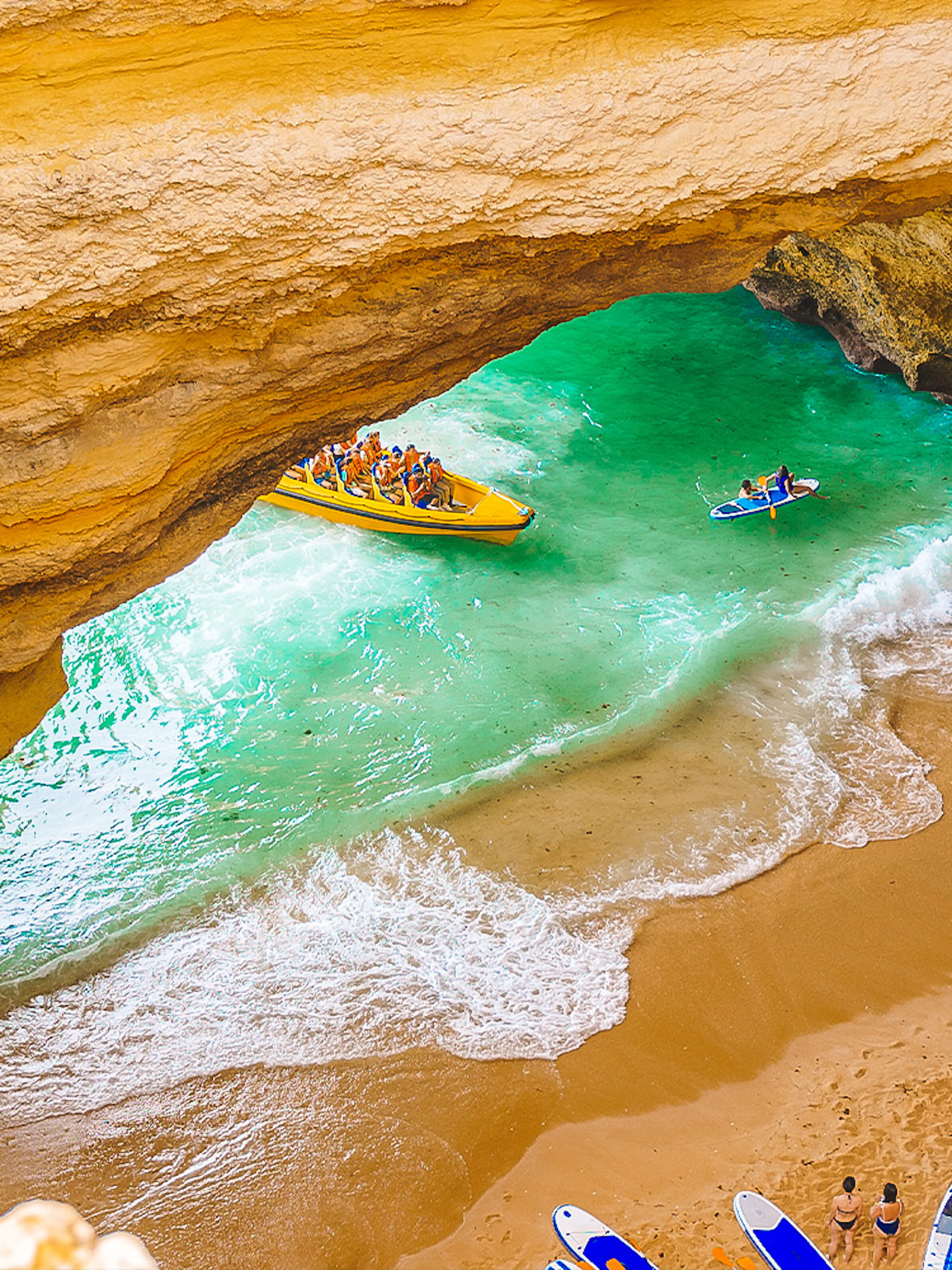 Boat tour entering Benagil Caves with people kayaking and paddleboarding on the beach.