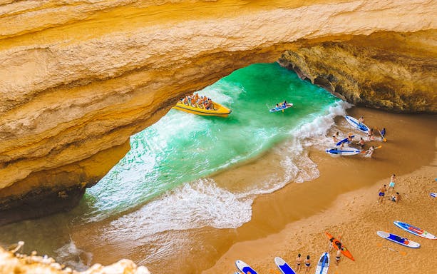 Boat tour entering Benagil Caves with people kayaking and paddleboarding on the beach.