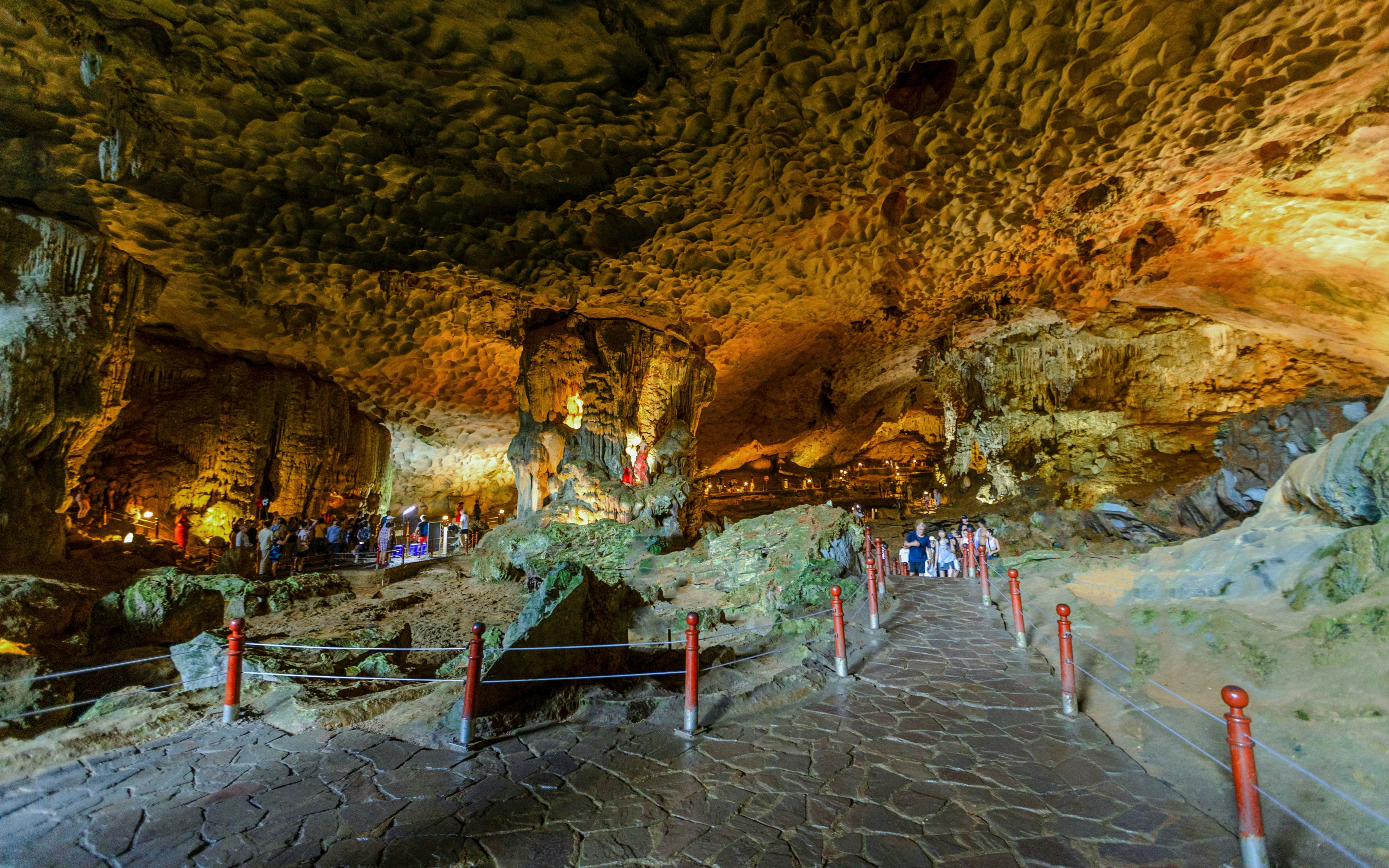 Visitors exploring Sung Sot Cave's illuminated formations, Ha Long Bay, Vietnam.
