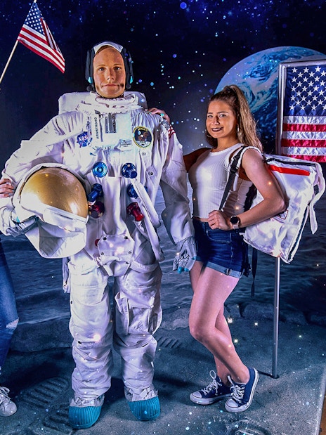 Neil Armstrong wax statue with visitors at Madame Tussauds, featuring lunar backdrop and American flag.