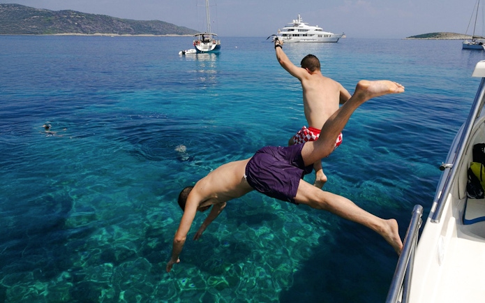 Tourists jumping from boat into clear water near Blue Cave, Croatia.