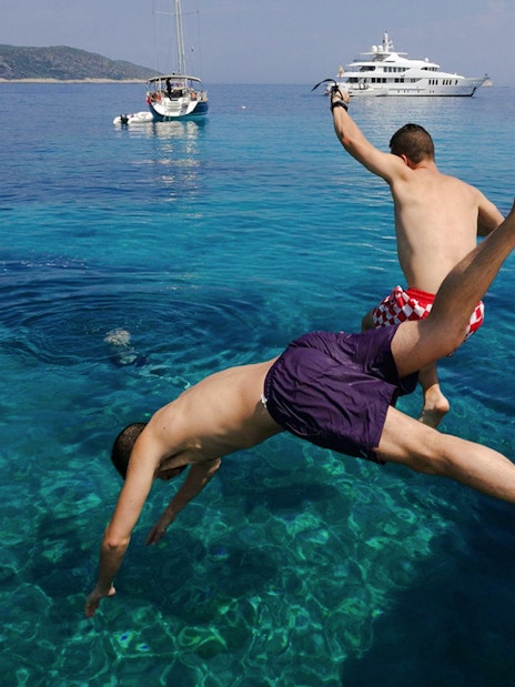 Tourists jumping from boat into clear water near Blue Cave, Croatia.