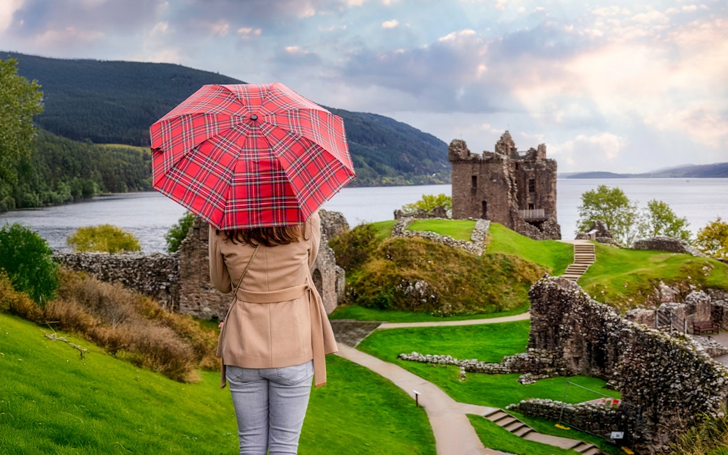Tourist with Scottish umbrella views Urquhart Castle at Loch Ness, Scotland in autumn.