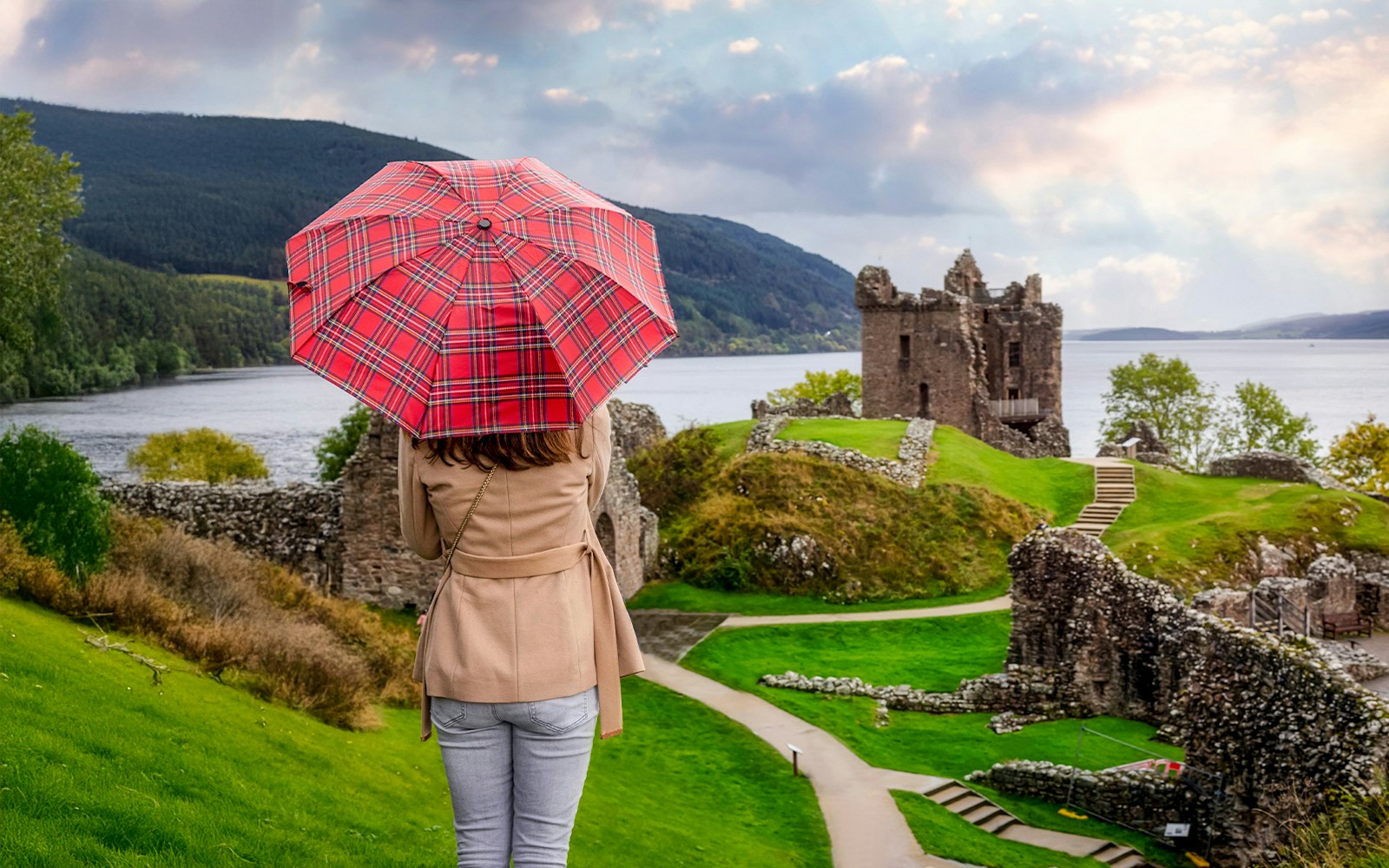 Tourist with Scottish umbrella views Urquhart Castle at Loch Ness, Scotland in autumn.