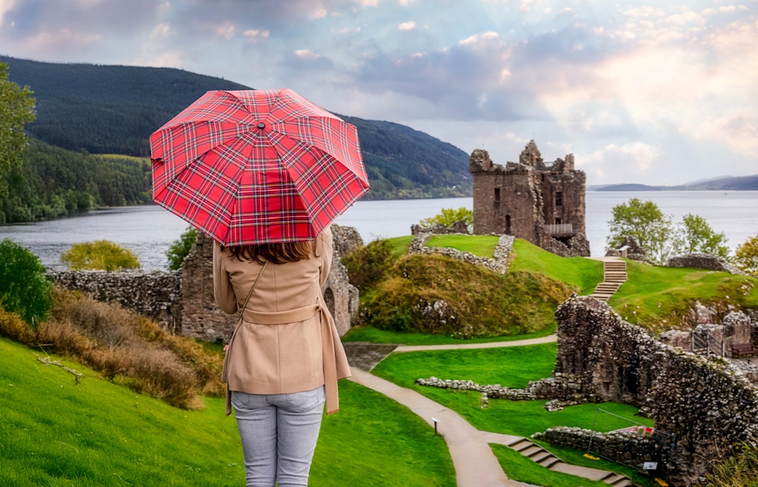 Tourist with Scottish umbrella views Urquhart Castle at Loch Ness, Scotland in autumn.