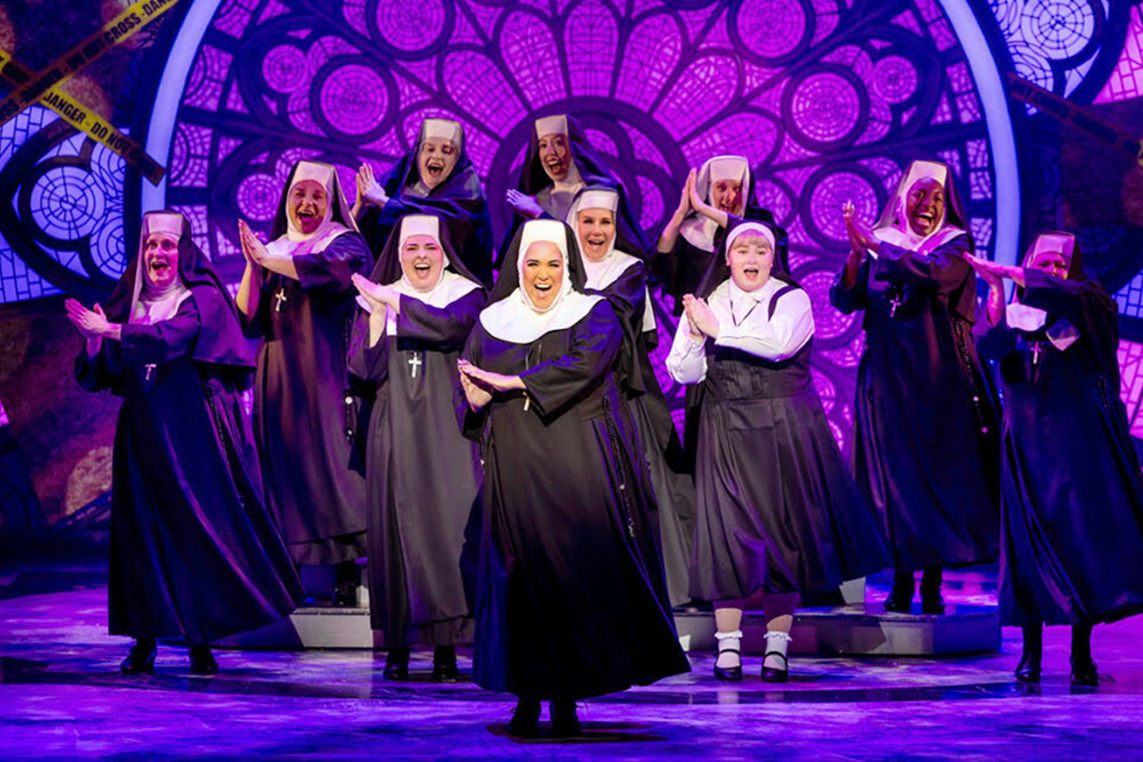 Nuns performing on stage in the musical "Sister Act" with a stained glass backdrop.