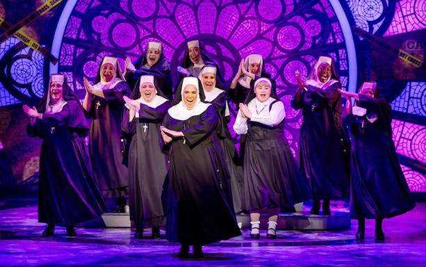 Nuns performing on stage in the musical "Sister Act" with a stained glass backdrop.