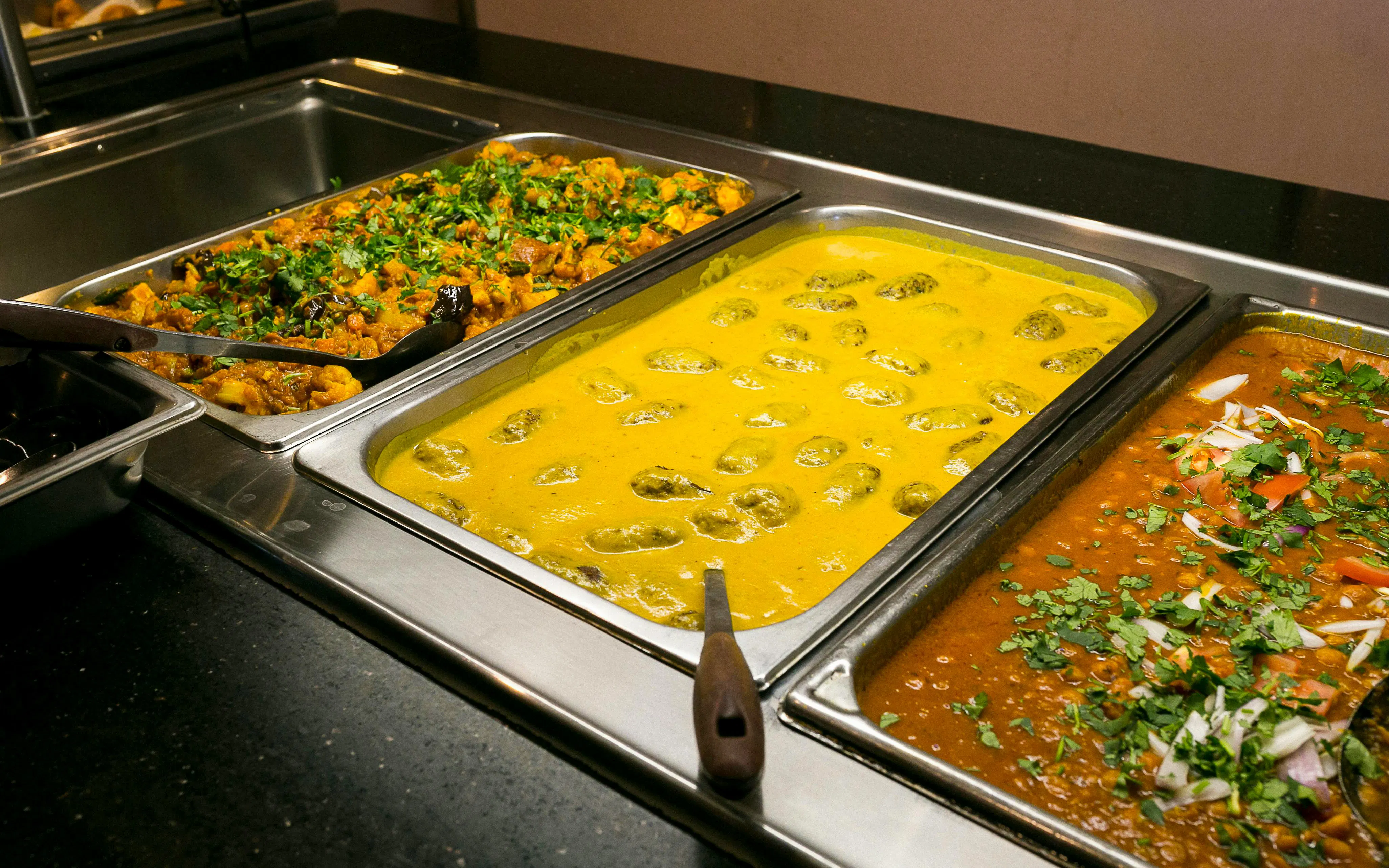 Indian buffet with yellow curry, vegetable curry, and lentil dish garnished with herbs.