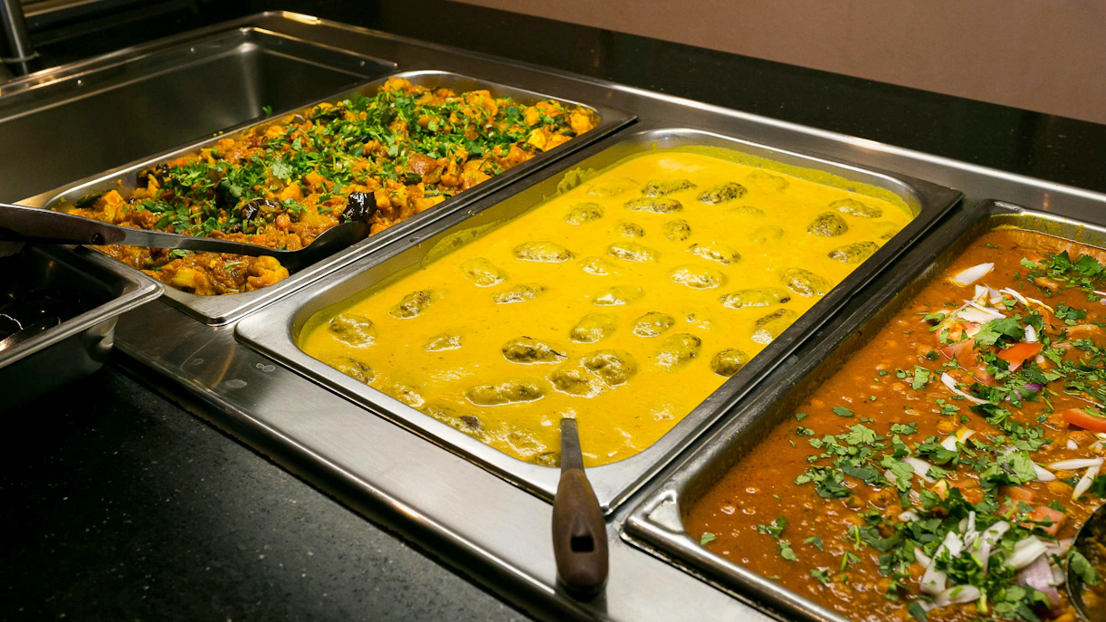 Indian buffet with yellow curry, vegetable curry, and lentil dish garnished with herbs.