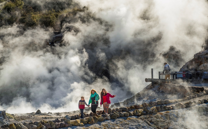 Tourists walking along steaming cliffs at Hells Gate Geothermal Walk.