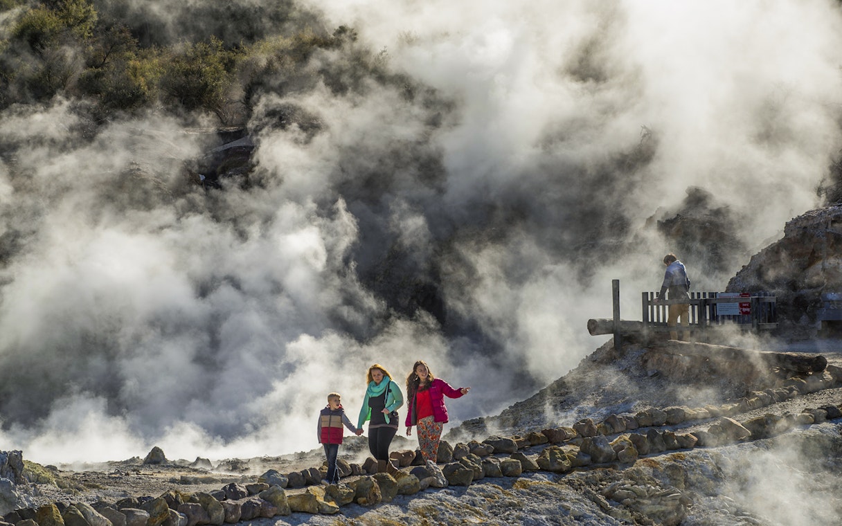 Tourists walking along steaming cliffs at Hells Gate Geothermal Walk.
