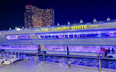 Luxury White Dinner Cruise docked at ICONSIAM, Bangkok, with illuminated decks and city skyline.