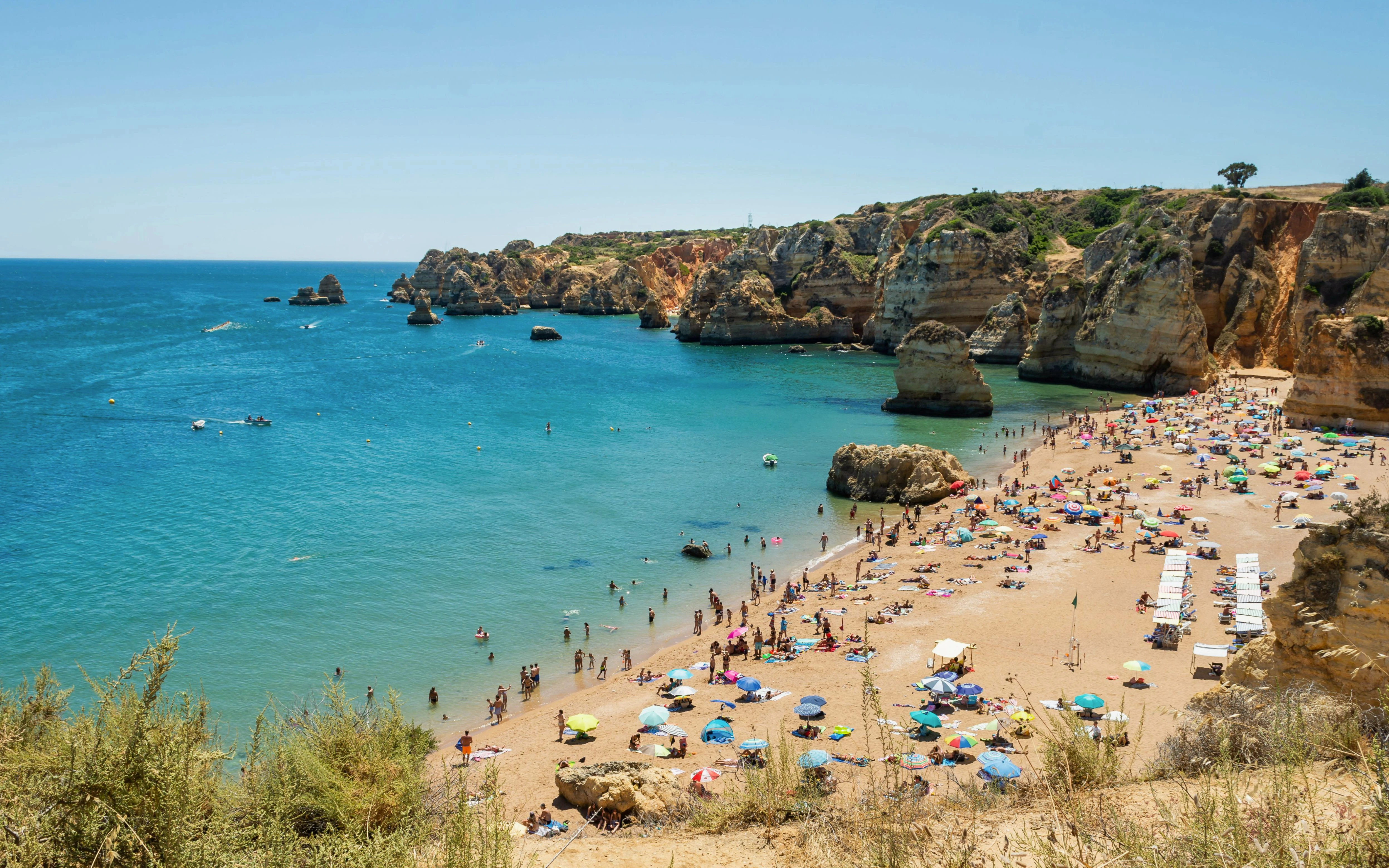 Beachgoers at Praia Dona Ana, Lagos, Portugal, with cliffs and turquoise water.