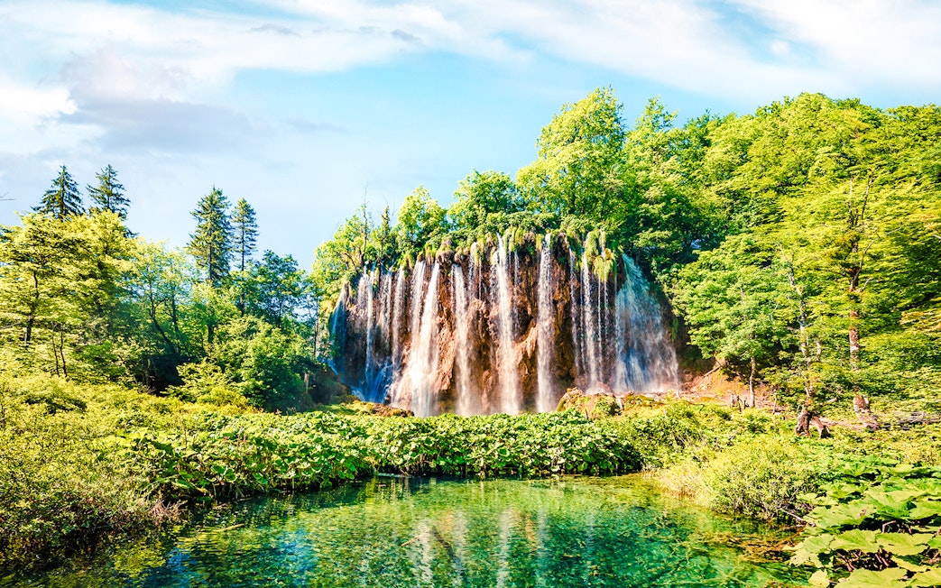 Waterfall cascading into a clear pool surrounded by lush greenery in Plitvice Lakes National Park.