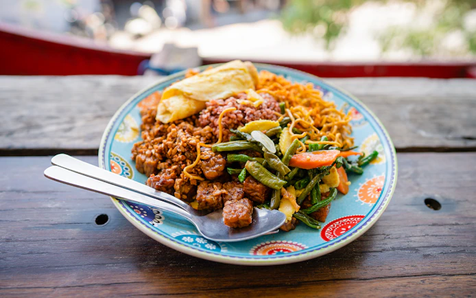 Plate of Indonesian food with rice, vegetables, and tempeh, served on a colorful dish.