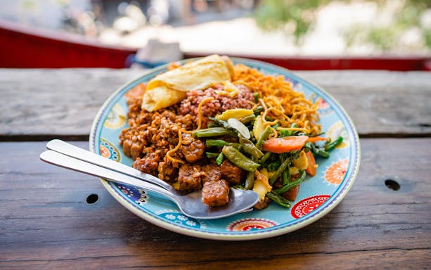 Plate of Indonesian food with rice, vegetables, and tempeh, served on a colorful dish.
