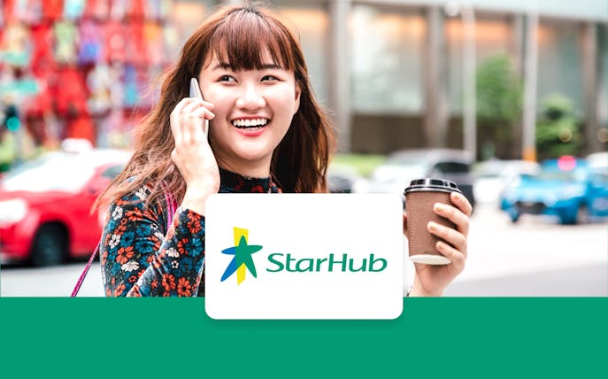 Person using phone with StarHub logo, holding coffee cup, city street background.