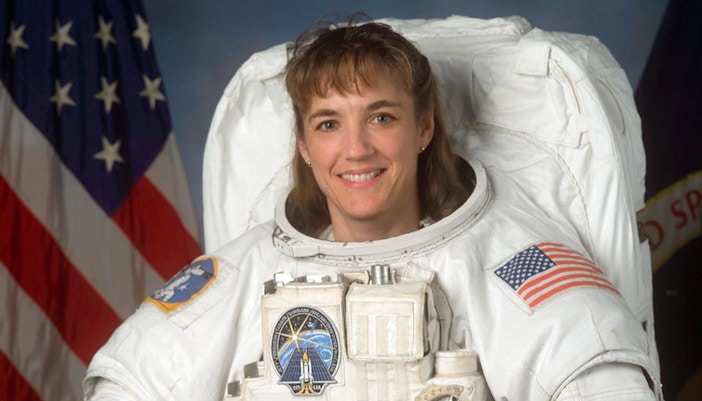 Heidi Piper in astronaut suit with helmet, space background.