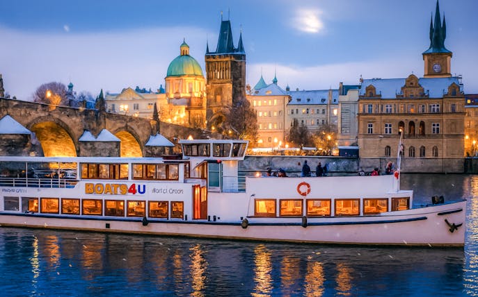 Cruise boat on Vltava River with Prague's Charles Bridge and historic buildings in the background.