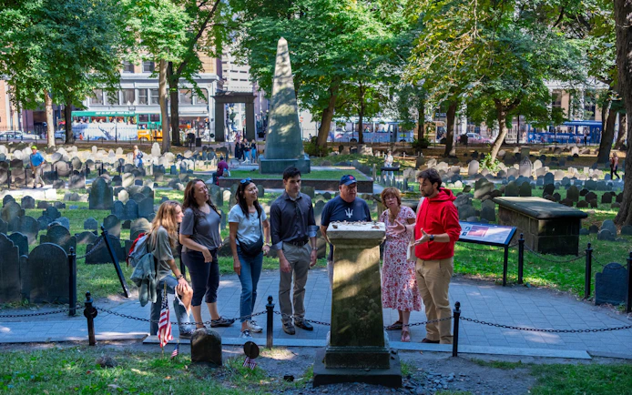 Tour group at Granary Burying Ground, Boston, Massachusetts, with historic gravestones and obelisk.