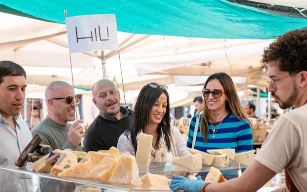 Tourists sampling cheese at a market stall during a street food tour in Palermo.