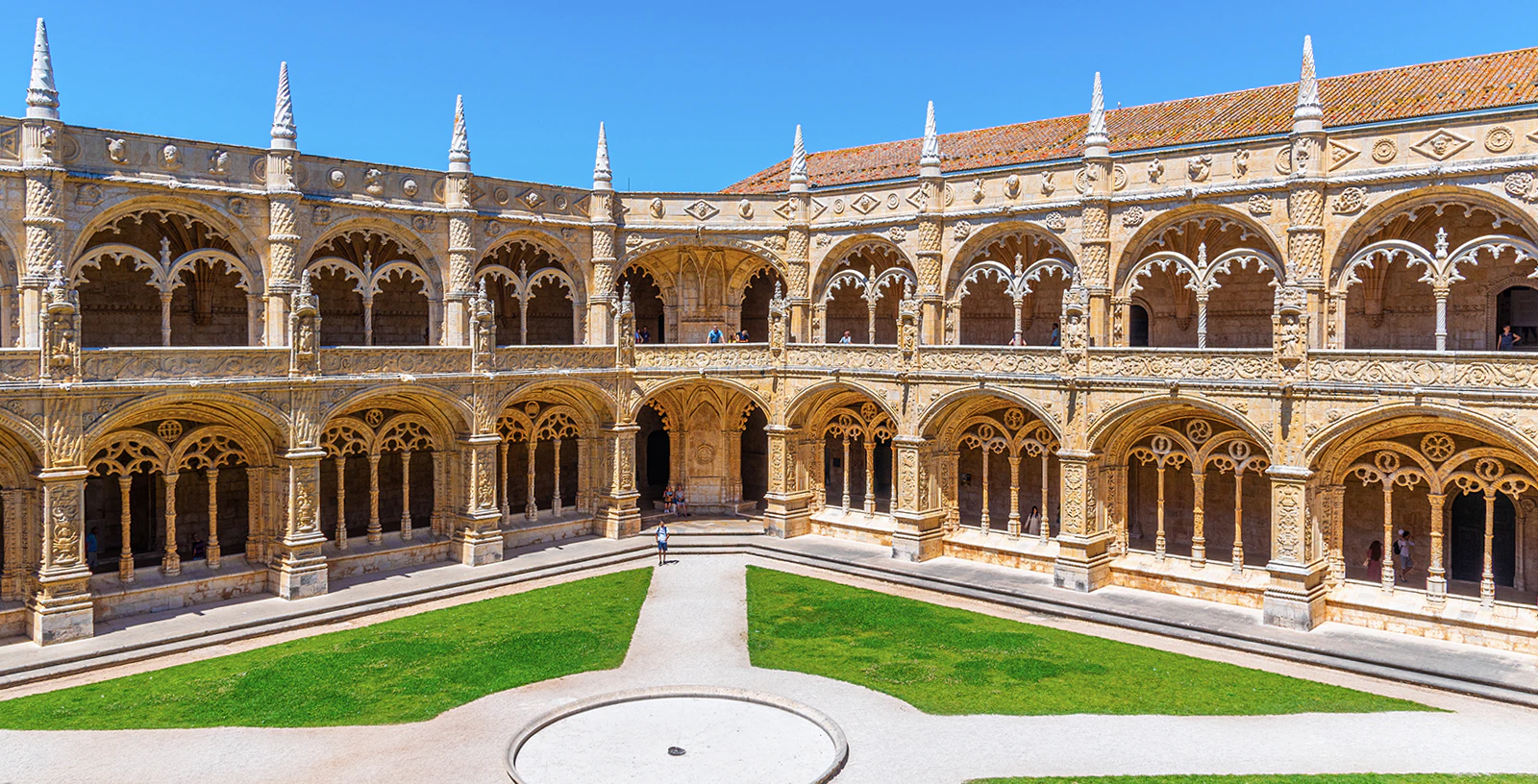Monastery of Jerónimos cloister with ornate arches and green courtyard in Lisbon, Portugal.