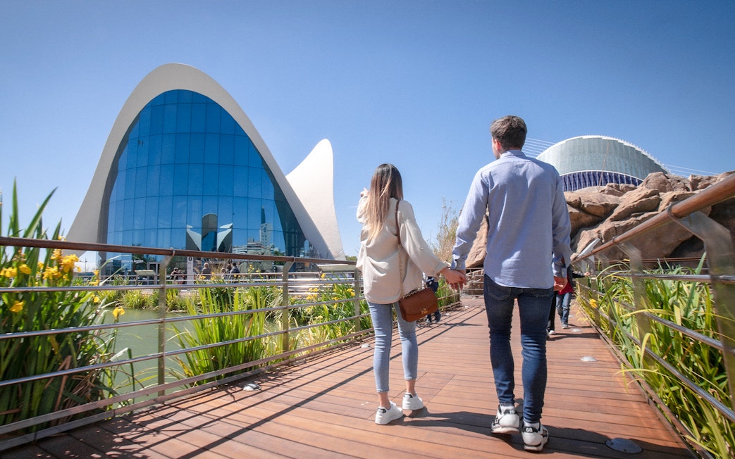 Couple walking towards Oceanogràfic Valencia, Spain, with modern architecture in view.