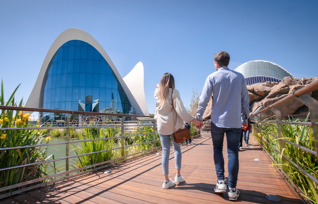 Couple walking towards Oceanogràfic Valencia, Spain, with modern architecture in view.